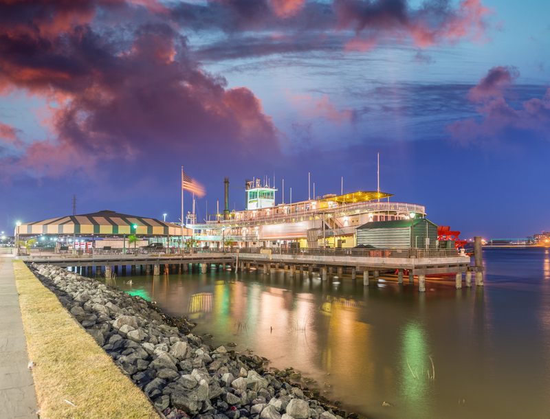 Steam paddlewheeler lit up at its wharf on the New Orleans riverfront at dusk, a landmark for paddle wheel boat cruises in New Orleans