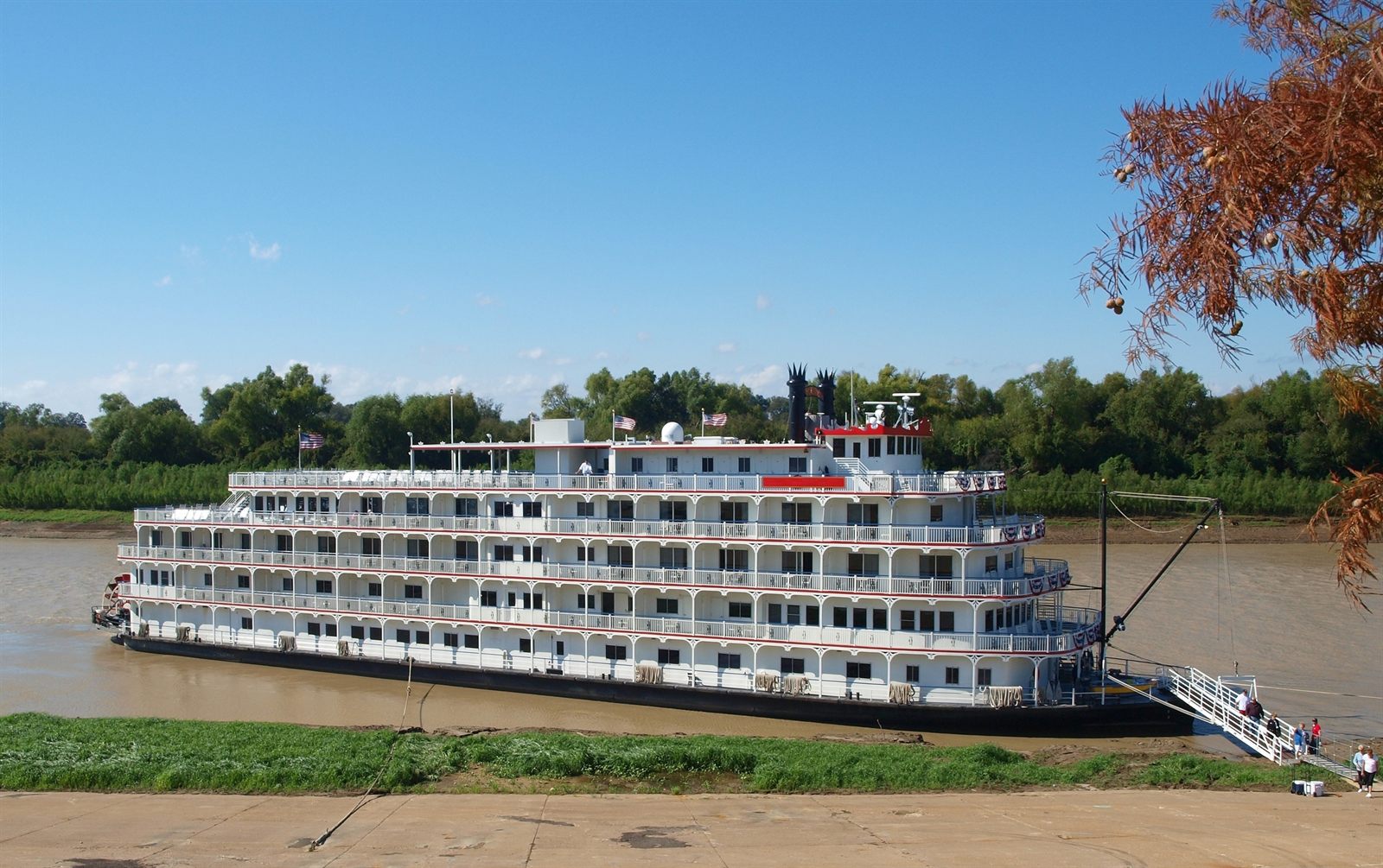 Older travelers walking down the gangway of a five-deck paddlewheel riverboat moored on the Mississippi, a popular style of Mississippi riverboat cruises for seniors